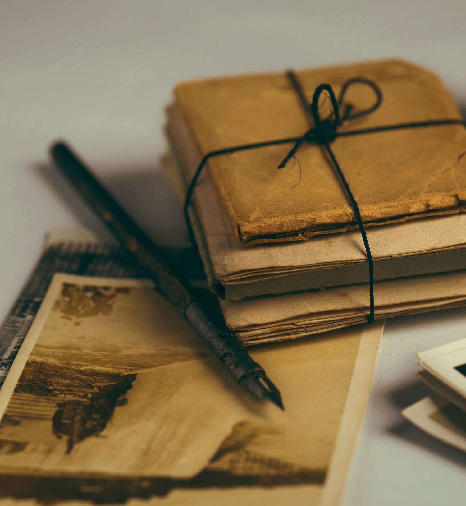 a stack of old papers, bound in black twine, sitting next to a fountain pen atop an old sepia-toned photograph (for Support Sorcery, business magic for witches, witchy assistant, blending magic and business)