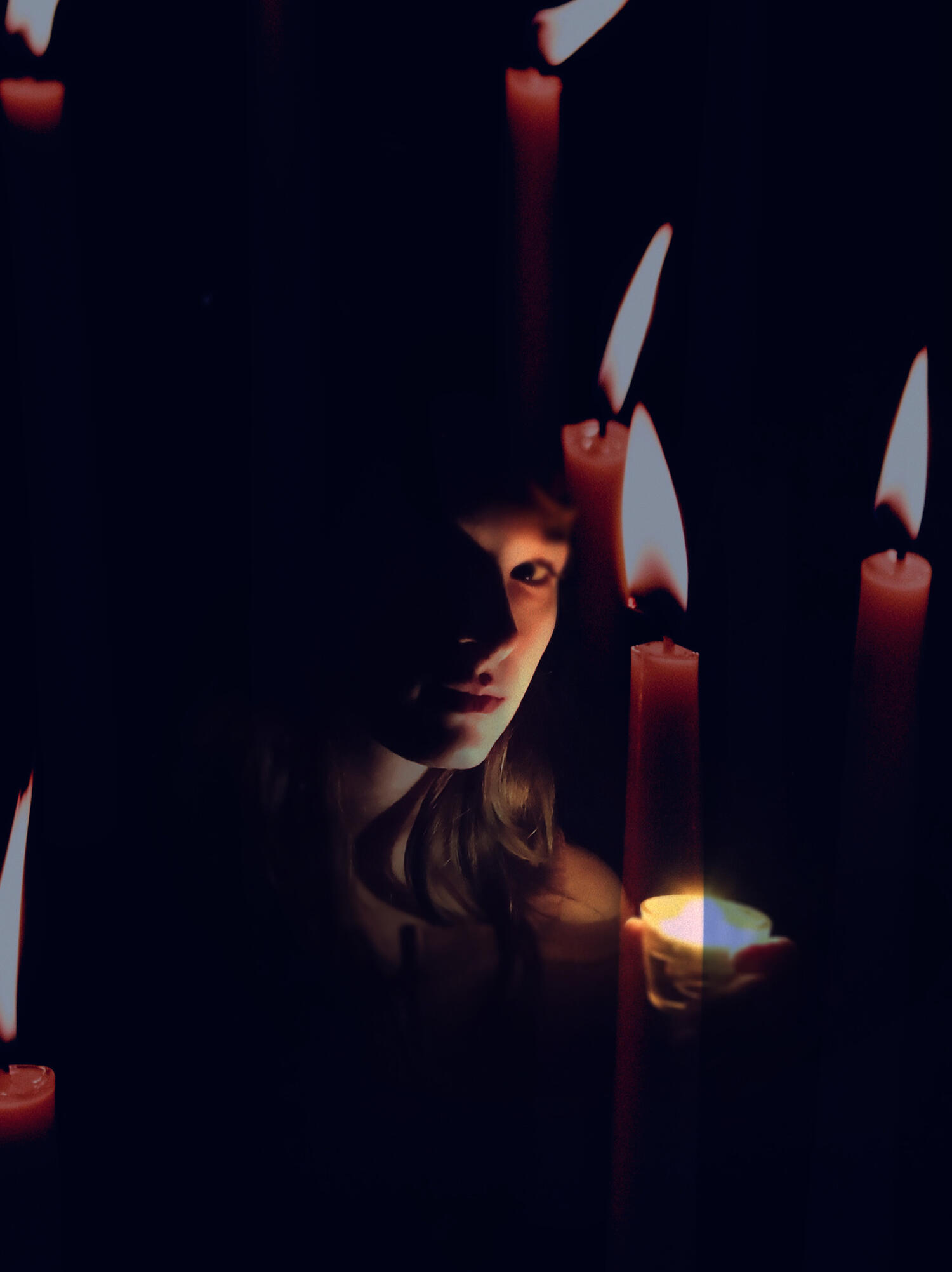 the professional magical witchy virtual assistant at Support Sorcery shrouded in darkness, with their face lit by candlelight, surrounded by opaque red candles